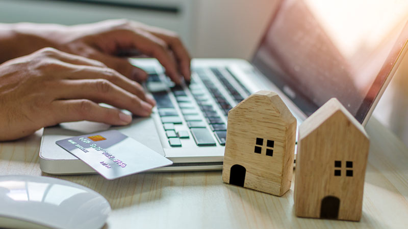 Pessoa a escrever no portátil, cartão de crédito e duas casas em madeira